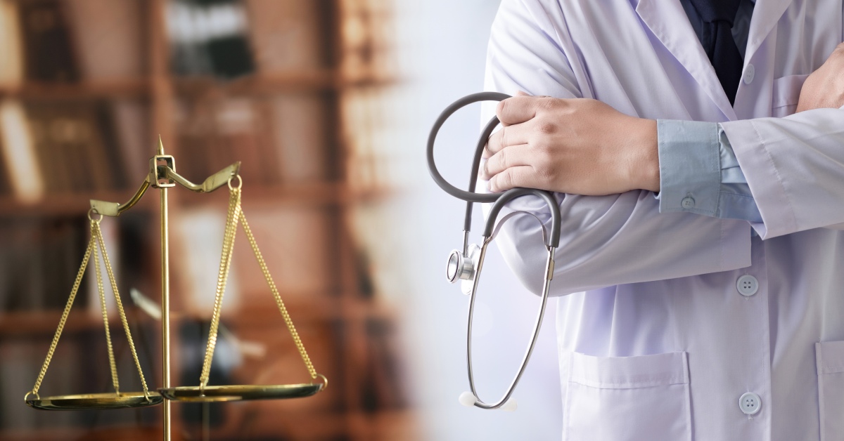 A nondescript doctor in a white lab coat holding a stethoscope, standing next to the golden scales of justice.