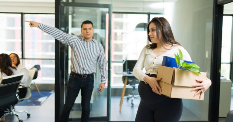 A man in a striped shirt points to the left of the image, looking at a pregnant woman as she holds a box of items.