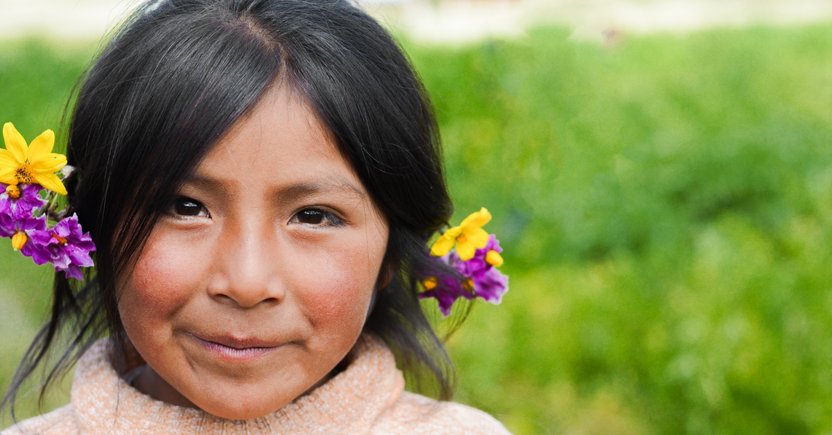 A Native American child with yellow and purple flowers in her hair. She is wearing a knitted pink turtleneck.