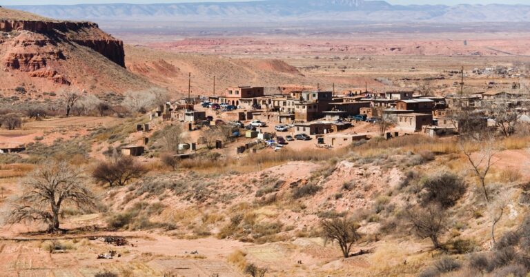 A long shot of a small suburban community in the middle of a sprawling desert with mesas in the background.