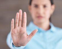 A close-up, focus shot of a woman's hand as she sticks it outward, palm facing the camera; she is blurred out in the background.