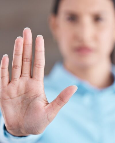 A close-up, focus shot of a woman's hand as she sticks it outward, palm facing the camera; she is blurred out in the background.