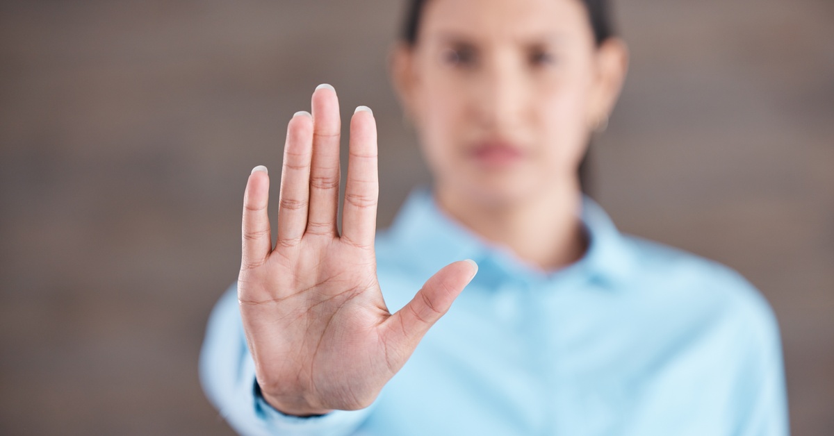 A close-up, focus shot of a woman's hand as she sticks it outward, palm facing the camera; she is blurred out in the background.