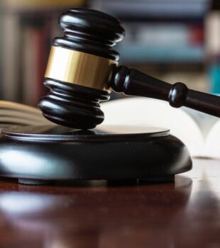 A dark, wooden gavel on top of a wooden block of the same color and material, next to several open books on a table.