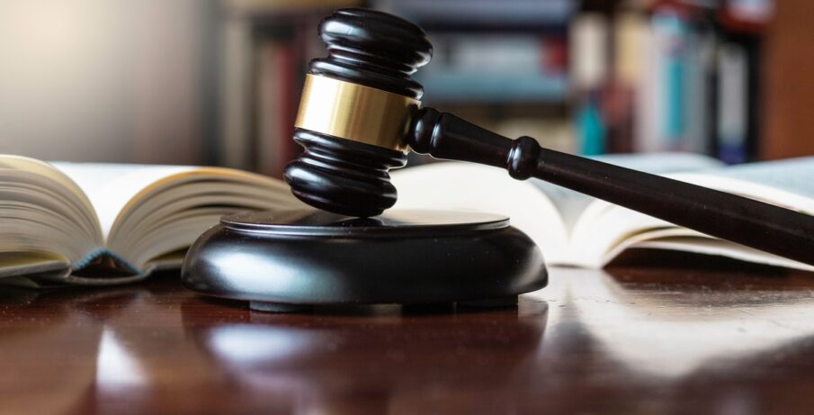 A dark, wooden gavel on top of a wooden block of the same color and material, next to several open books on a table.