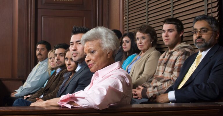 Twelve individuals of varying genders and ages seated in a designated wooden section near a door marked 