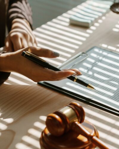 Two people sitting at a desk that has a gavel and a scale of justice on it, holding pencils and pointing at a paper.