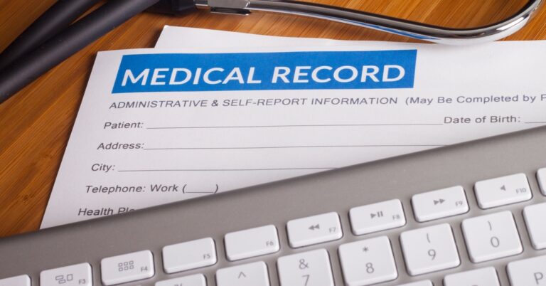 A document titled 'Medical Record' on a desk, partially hidden under a keyboard, with a stethoscope resting nearby.