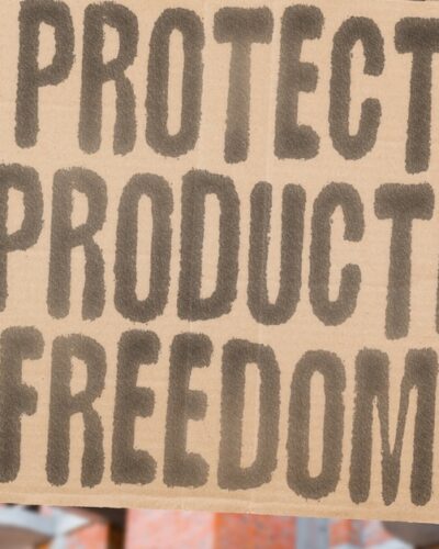 A person standing in front of a row of buildings, holding a cardboard sign with the message 