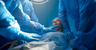 A woman dressed in a gown and hair net lying on a surgical table, surrounded by several other people in full scrubs.