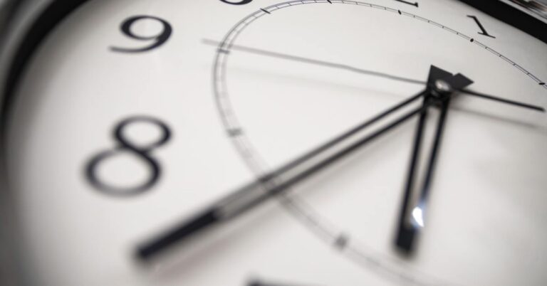 A round analog clock face shown in extreme close-up, with black hands and numbers curving outward from a white dial.