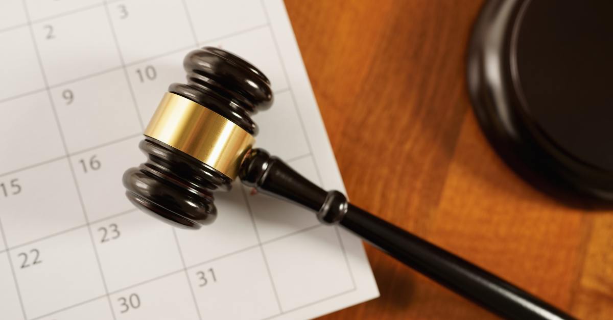 A wooden judge's gavel resting on a paper calendar page, with the band and numbered date squares in view.