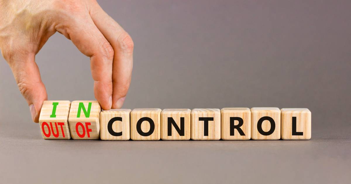 A hand placing or holding wooden cubes with the words in control and out of control arranged on a table.