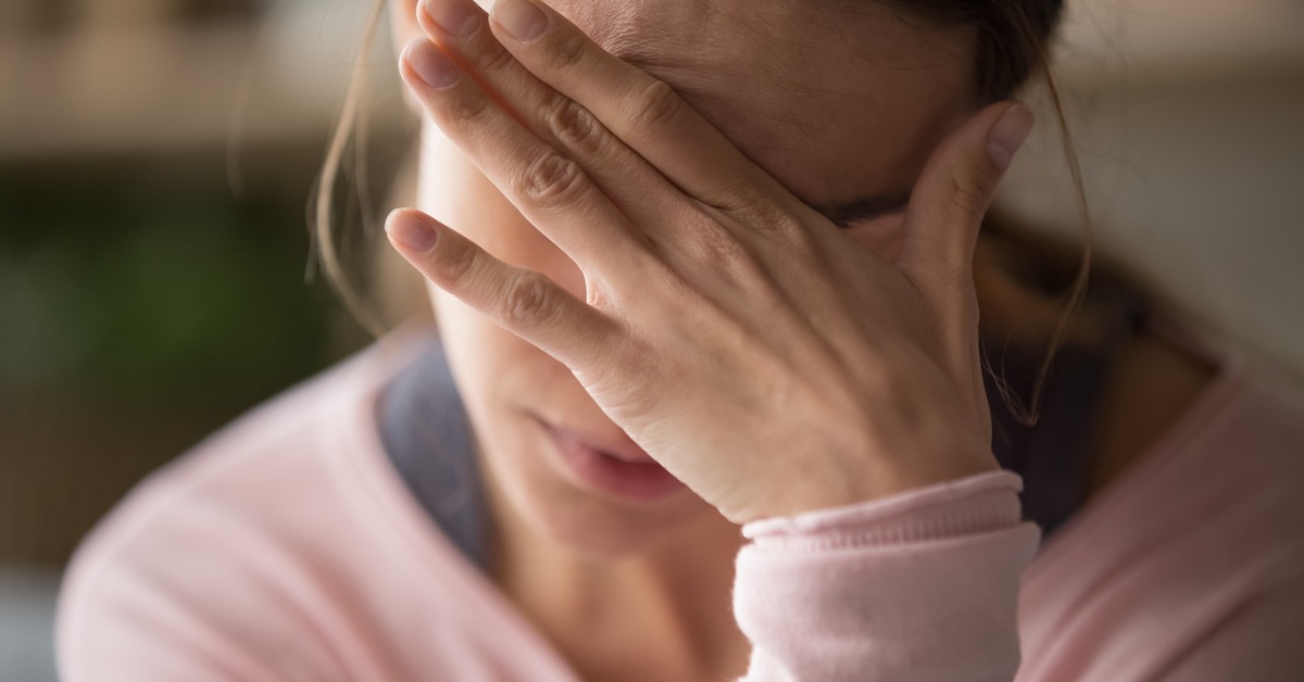 A woman touching her face with her hand while sitting with her eyes closed and head slightly lowered.