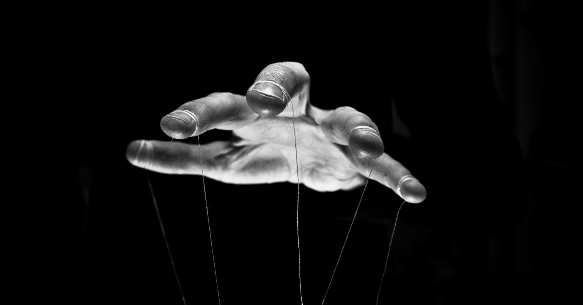 A hand, in monochrome, facing down with the fingers spread out. There are marionette strings attached to each finger.