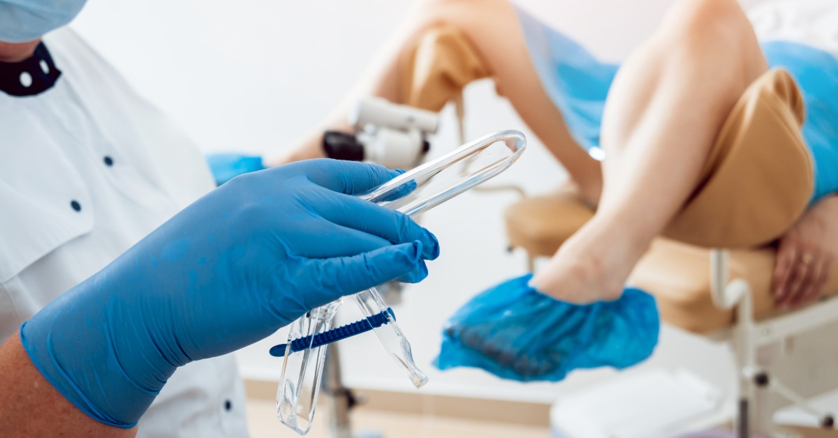 A woman reclining in an examination chair while another person uses medical equipment nearby in a OBGYN office.