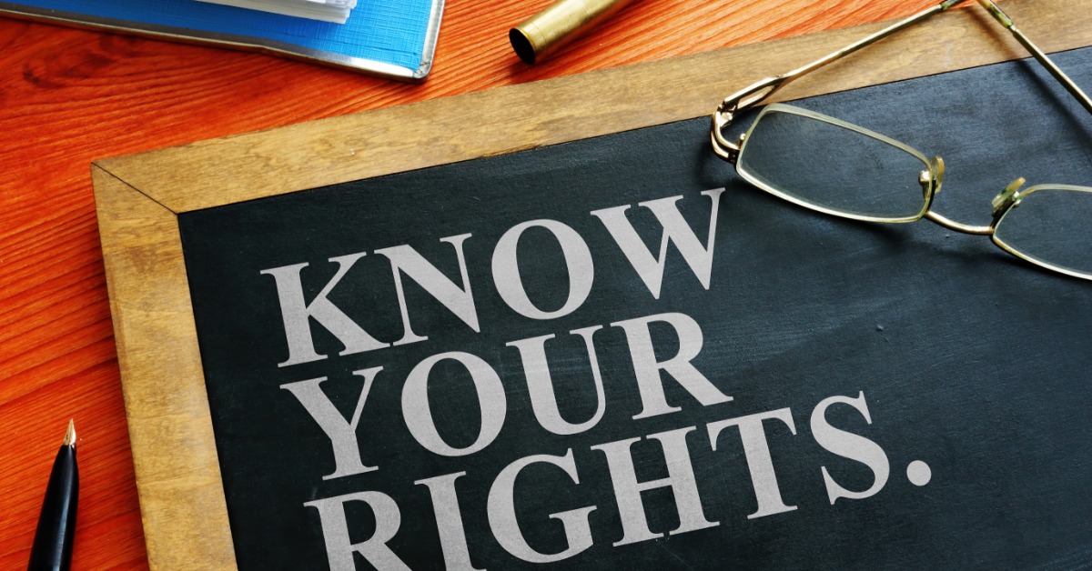 A notebook, uncapped pen, eyeglasses, and wooden sign reading know your rights arranged on a desk surface.