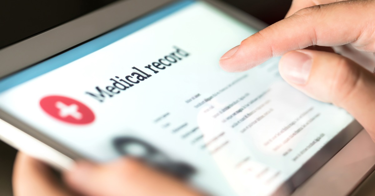 A tablet showing a medical record screen while a hand points near patient information and a red health icon.