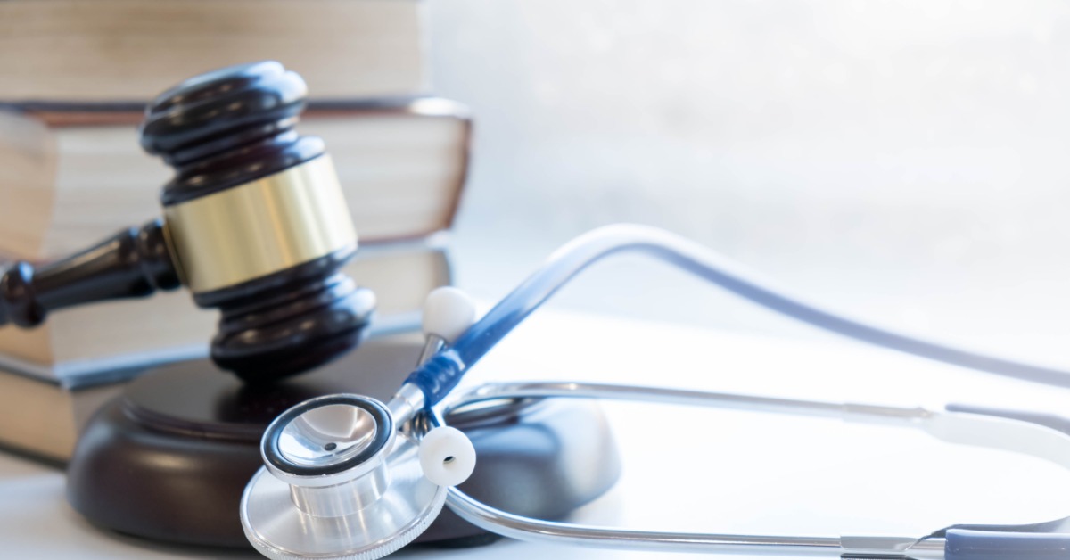 A gavel beside stacked books and a stethoscope resting on a bright white surface with soft light in the background.