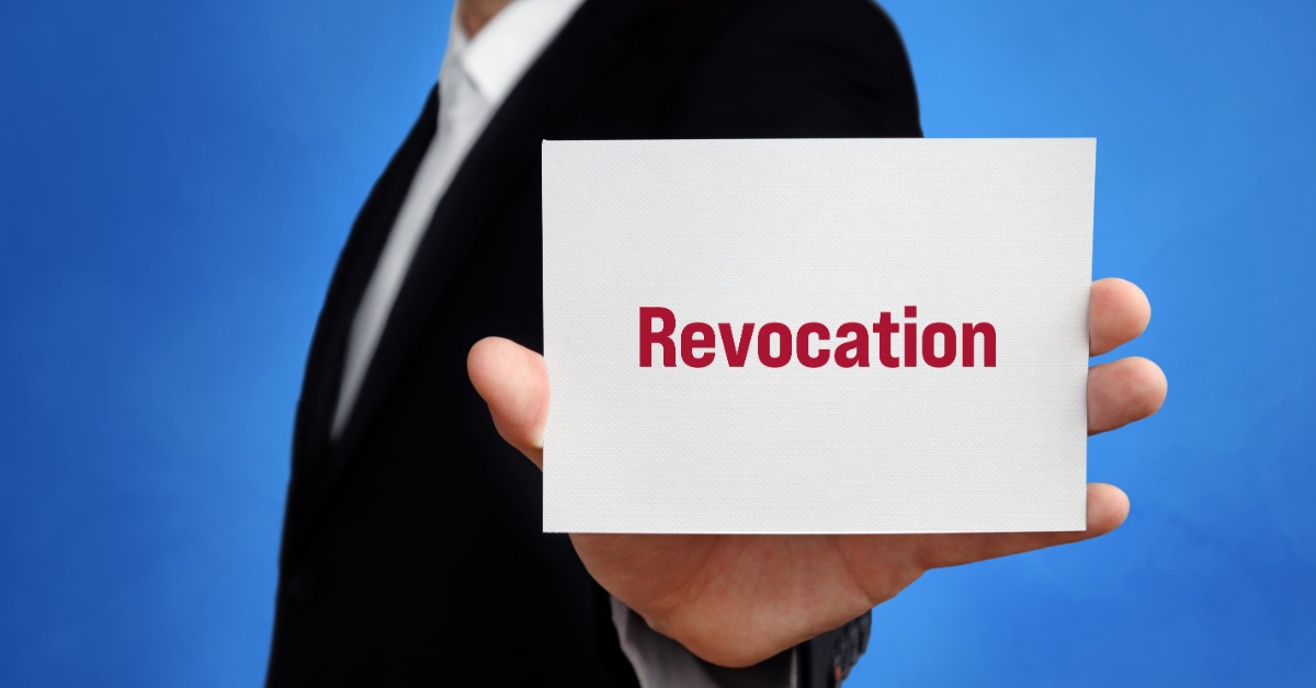A person in a dark suit holding a white card with the word revocation in red against a blue background. A person in a dark suit holding a white card with the word revocation in red against a blue background.