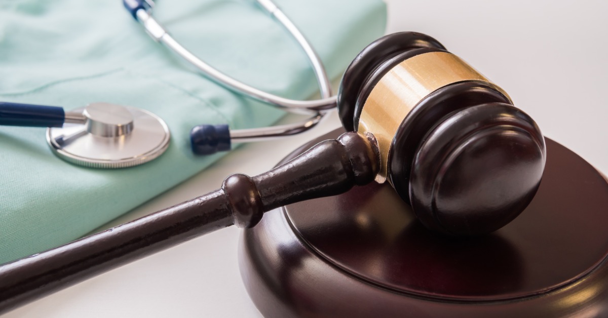 A wooden gavel resting on a round base beside a stethoscope and folded green fabric on a light surface. A wooden gavel resting on a round base beside a stethoscope and folded green fabric on a light surface.