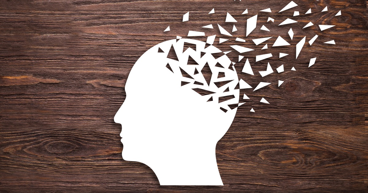 A white head silhouette with fragmented pieces breaking away from the upper right side against a dark wood background.