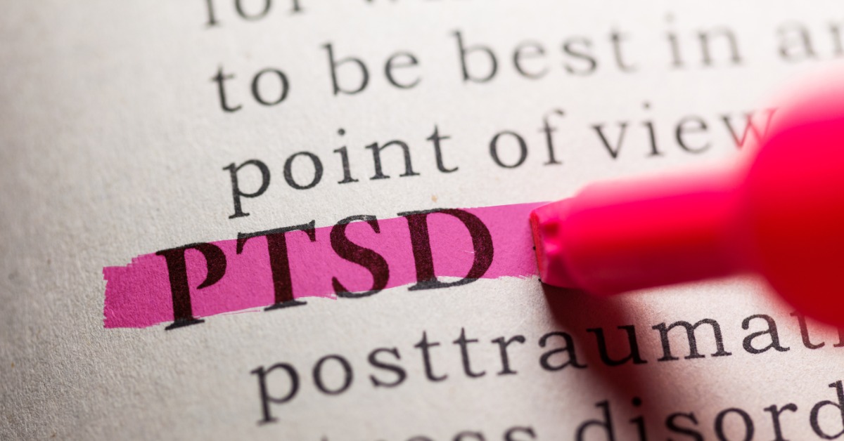 A red highlighter marking the letters PTSD on a printed dictionary page, with surrounding words out of focus.